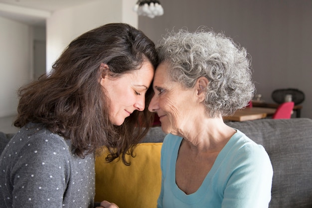 Adult daughter and old mother touching foreheads