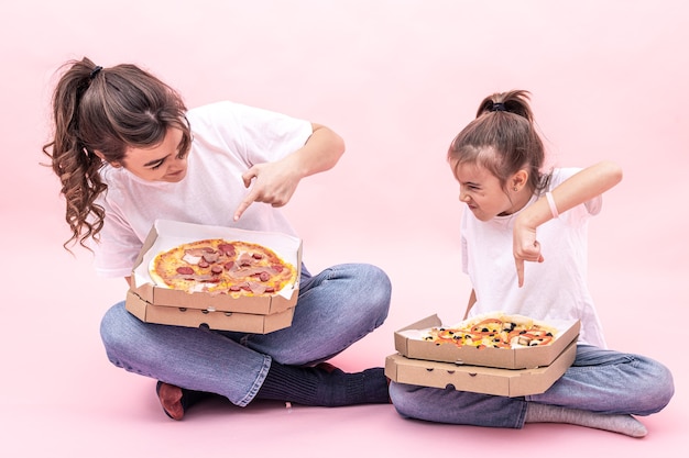 Free photo an adult girl and a little girl with different pizzas in boxes, pink background.