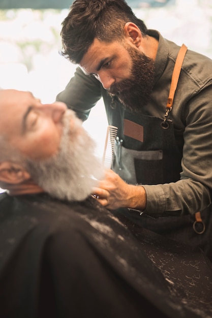 Free photo adult hairdresser shaving customers beard at hair salon