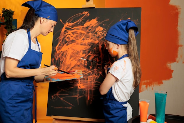 Free Photo adult and kid using orange paint on canvas