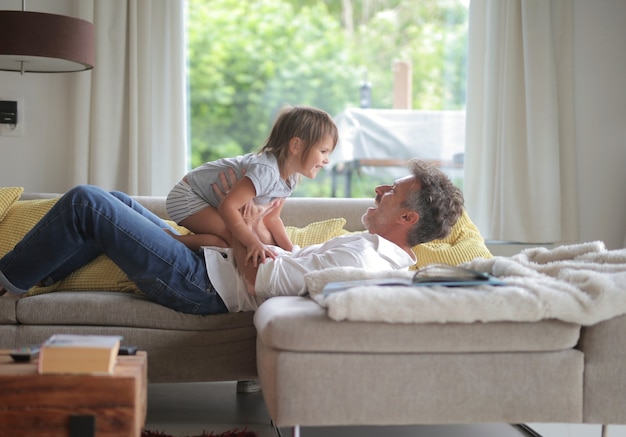 Adult male lying on the sofa and playing with his child under the sunlight through the windows