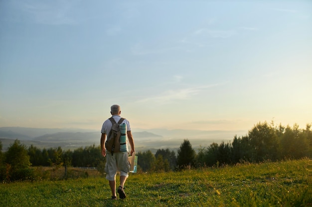 Free photo adult male traveler walking along green hill while backpacking in mountains