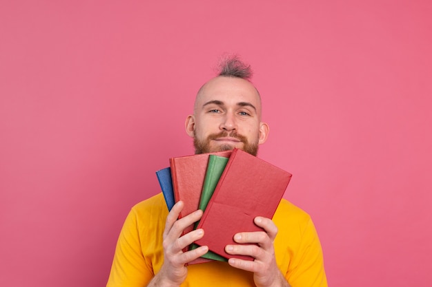 Free Photo adult smiling casual clothes guy with beard hugs favorite books to himself isolated on pink