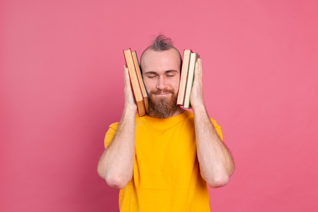 Free photo adult smiling casual clothes guy with beard hugs favorite books to himself isolated on pink