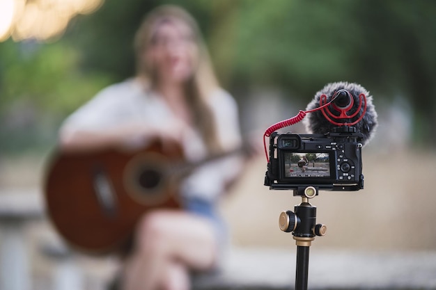 Free photo adult woman playing the acoustic guitar in a park and recording herself with a dslr camera