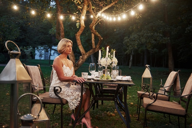 Free photo adult woman sits on the chair with candles and wine glasses in the outdoor part of restaurant