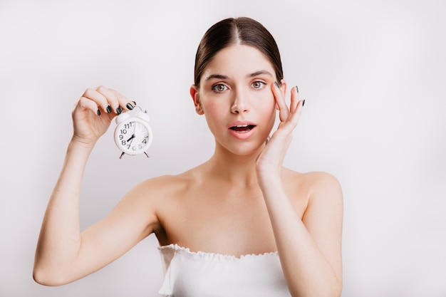 Adult woman with elastic healthy skin, holding small white alarm clock.