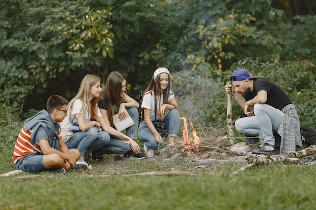 Adventure, travel, tourism, hike and people concept. Group of smiling friends in a forest. People sitting near bonfire.