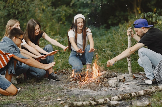 Free Photo adventure, travel, tourism, hike and people concept. group of smiling friends in a forest. people sitting near bonfire.