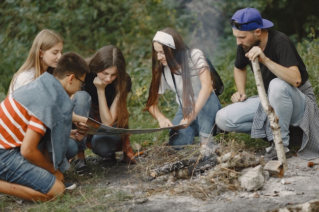 Adventure, travel, tourism, hike and people concept. Group of smiling friends in a forest. People sitting near bonfire.