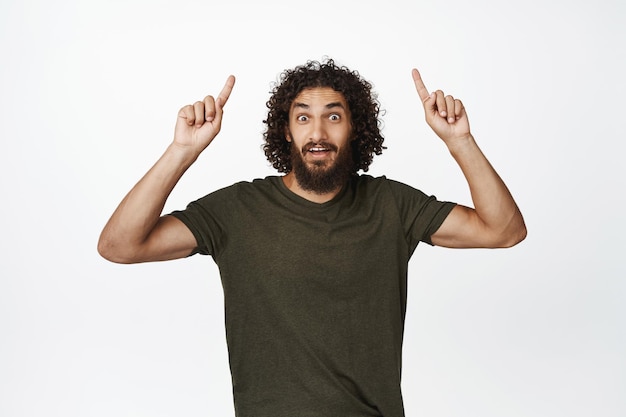 Advertisement Happy smiling man pointing fingers up showing promo offer sale banner upwards standing in tshirt over white background