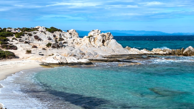 Aegean sea coast with greenery around, rocks and bushes, blue water with waves, Greece