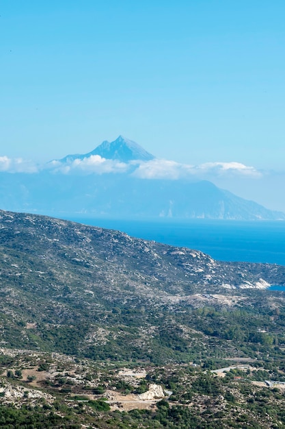 Aegean sea coast with hills full of greenery, buildings near the coast with high mountain reaching the clouds Greece