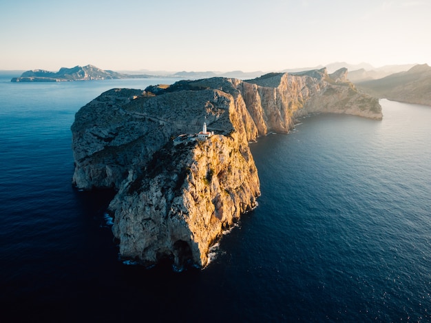 Aerial distant shot of a high rocky cliff with a white tower built on top in the middle of the ocean