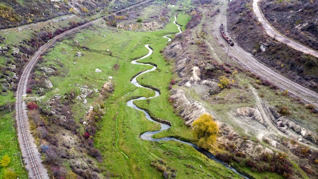 Aerial drone view of nature in Moldova, stream the stream flowing into the ravine, slopes with sparse vegetation and rocks, moving train, cloudy sky