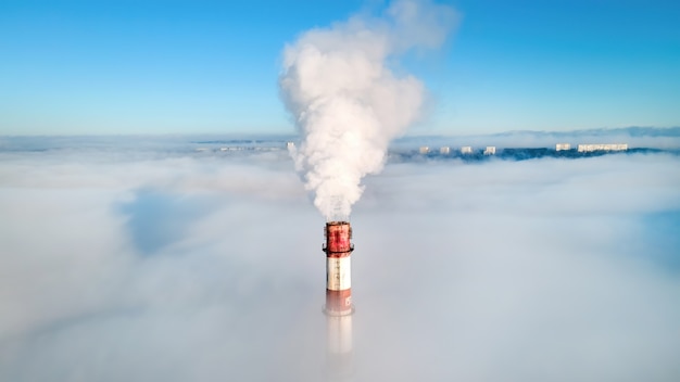 Free photo aerial drone view of thermal station's tube visible above the clouds with smoke coming out.