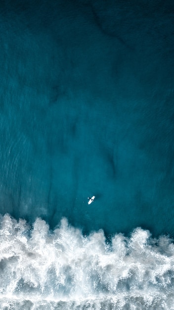 Free photo aerial overhead vertical shot of beautiful ocean waves with a plane flying above