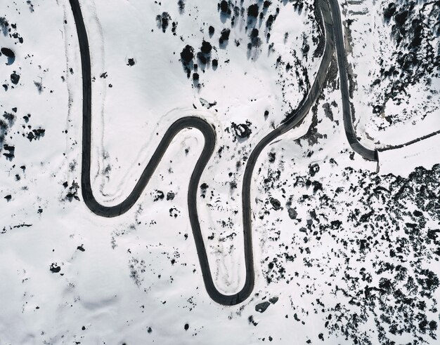 Aerial shot of a beautiful snowy field with a curved road in the middle