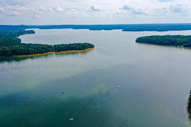 Free photo aerial shot of boats travelling across the lake with trees and a cloudy sky