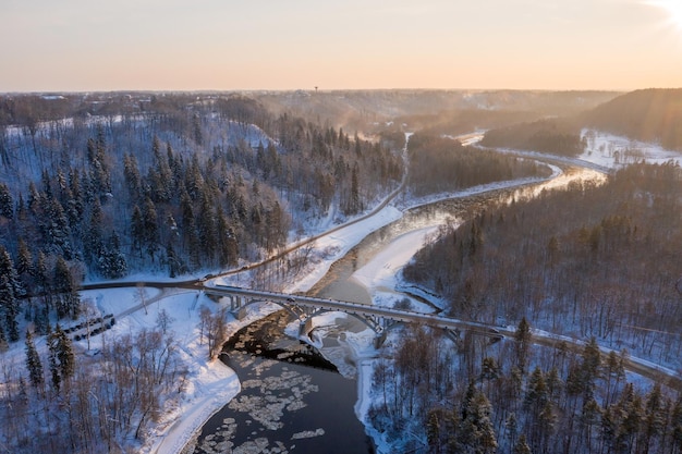 Free photo aerial shot of a curvy road over a flowing river through the snow-covered forest