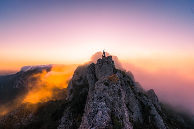 Free Photo aerial shot of a female with hands up on the top of the mountain at sunset