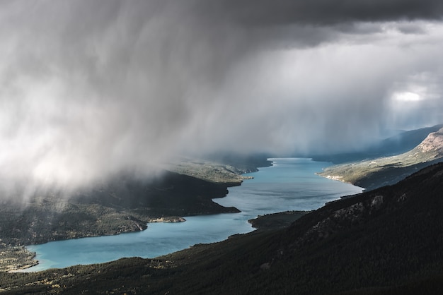 Aerial shot of a forested mountain near a river under a foggy sky