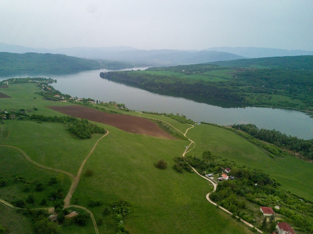 Aerial shot of the green landscapes, fields and a river under the cloudy sky on a sunny day