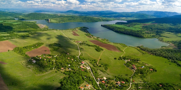 Aerial shot of the green landscapes, fields and a river under the cloudy sky on a sunny day