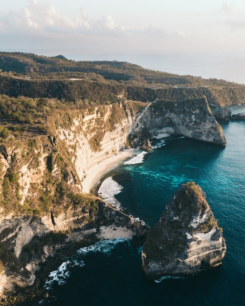 Free photo aerial shot of the ocean surrounded by the high mountains covered in greens