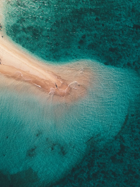 Aerial shot of the ocean waves hitting the small sandy island