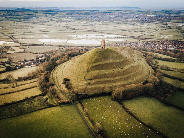 Aerial shot of an old castle on top of a grass-covered hill in the middle of the green fields