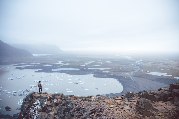 Free photo aerial shot of a person standing on a cliff overlooking the lakes in the fog captured in iceland