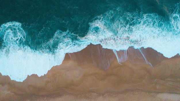 Aerial shot of sea waves hitting the sandy shore