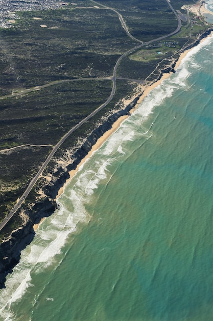 Free photo aerial vertical shot of a road in the middle of grassy fields near a beach shore