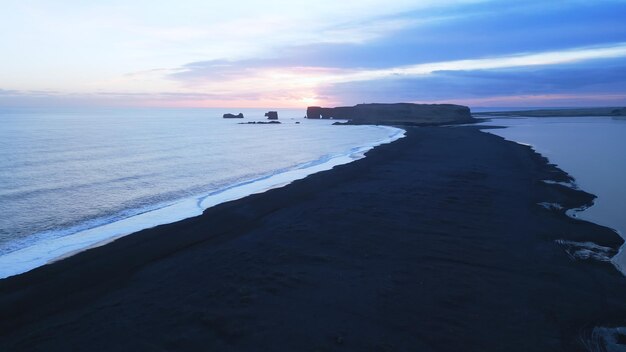 Aerial view of black sand beach with mountains and big stones in iceland, beautiful natural scenery on reynisfjara beach. Icelandic landscape with atlantic ocean on coastline. Slow motion.