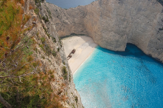 Free photo aerial view of the blue ocean surrounded by cliffs with the remnants of an old boat in the shore