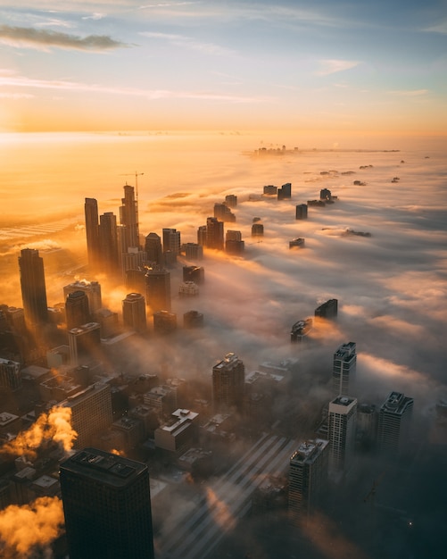 Free photo aerial view of a cityscape with tall skyscrapers during sunset covered with white clouds