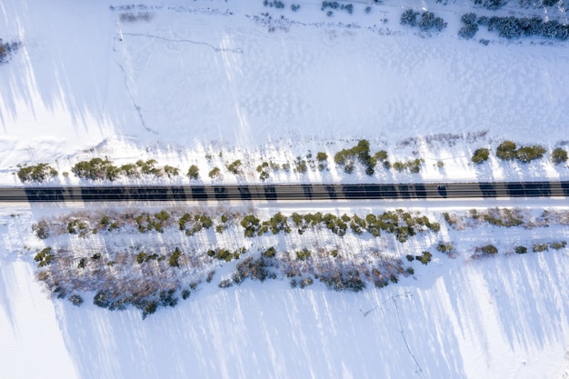 Free photo aerial view of a road surrounded by trees and snow under the sunlight