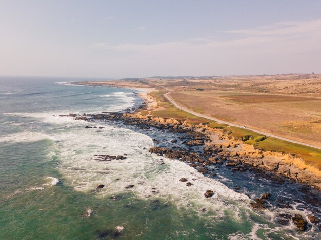 Aerial view of the wavy ocean hitting the rocky cliffs on the Pacific Ocean in California