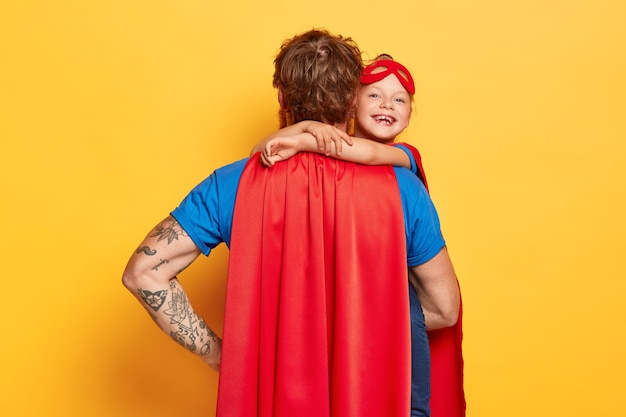 Free photo affectionate daddy wears red cape, stands back to camera