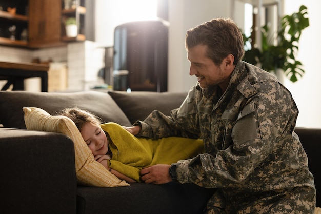 Free photo affectionate soldier looking at his sleepy daughter who is lying on the sofa at home