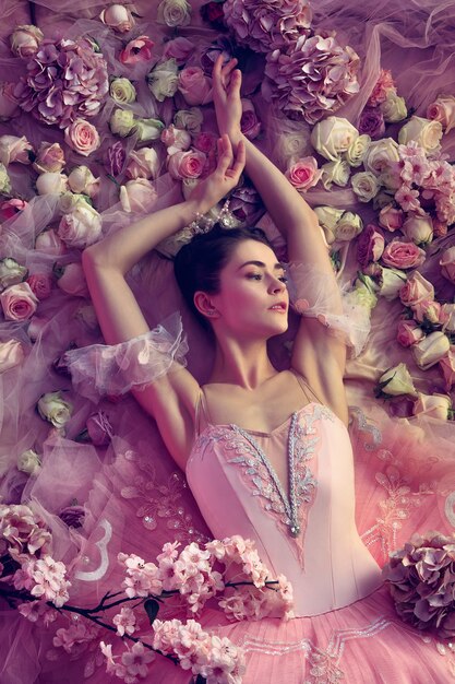 Affectivity. Top view of beautiful young woman in pink ballet tutu surrounded by flowers. Spring mood and tenderness in coral light. Concept of spring, blossom and nature's awakening.