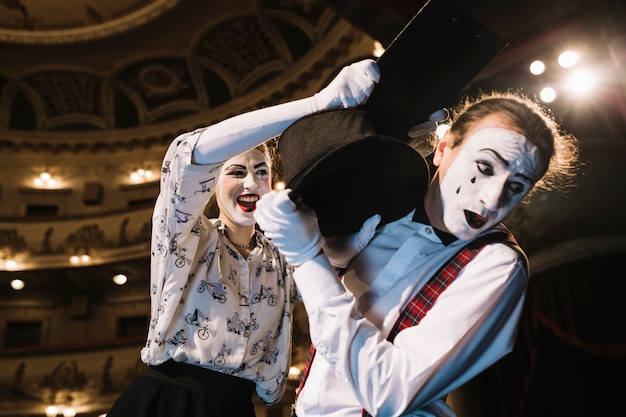 Afraid male mime defending from female mime hitting with clipboard