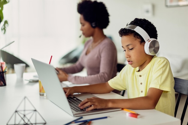 African American boy using laptop while his mother is working in the background