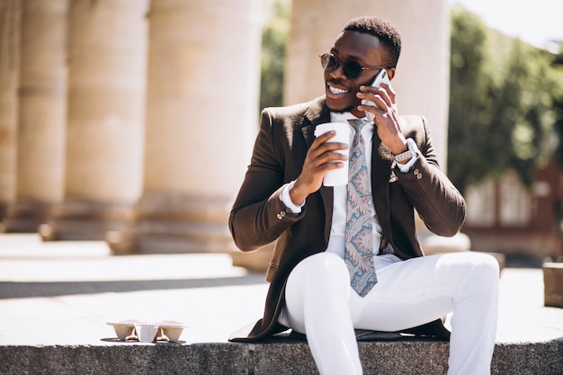 African american business with coffee and phone sitting on the stairs of a building