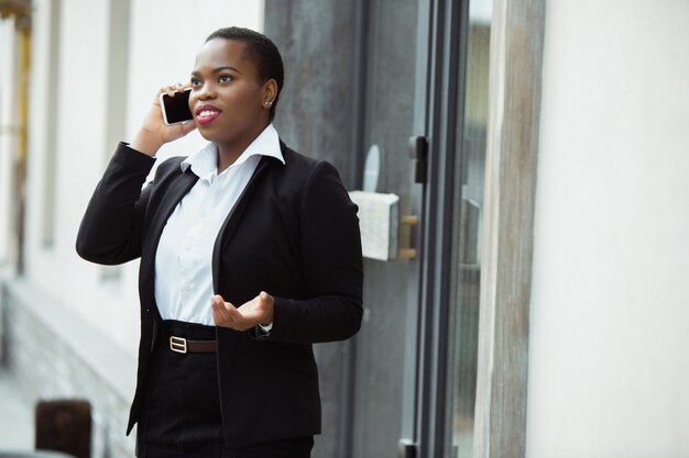 African American businesswoman in office attire smiling, looks confident and happy, busy