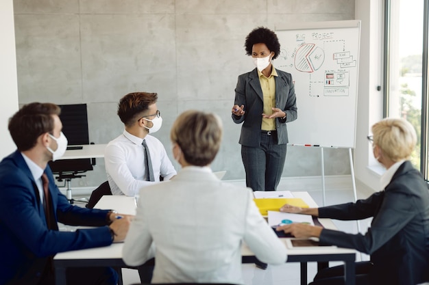 Free photo african american businesswoman with face mask giving presentation on a meeting in the office