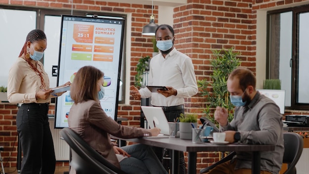 African american coworkers showing financial analysis on display, doing charts presentation in meeting office. Business people using monitor to design marketing project and startegy.