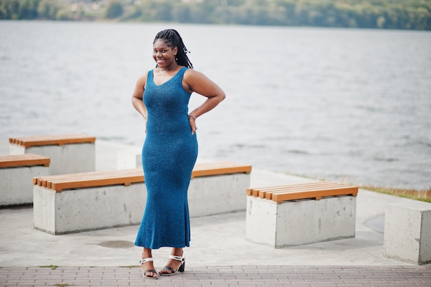 Free photo african american dark skinned plus size model posed in a blue shiny dress against sea side