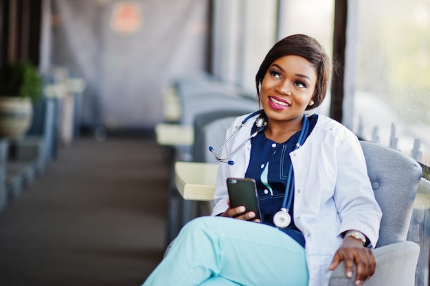 African american doctor female with stethoscope looked at phone and sitting on clinic